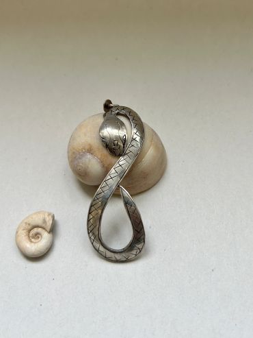 Colgante de serpiente metálica junto a conchas marinas.