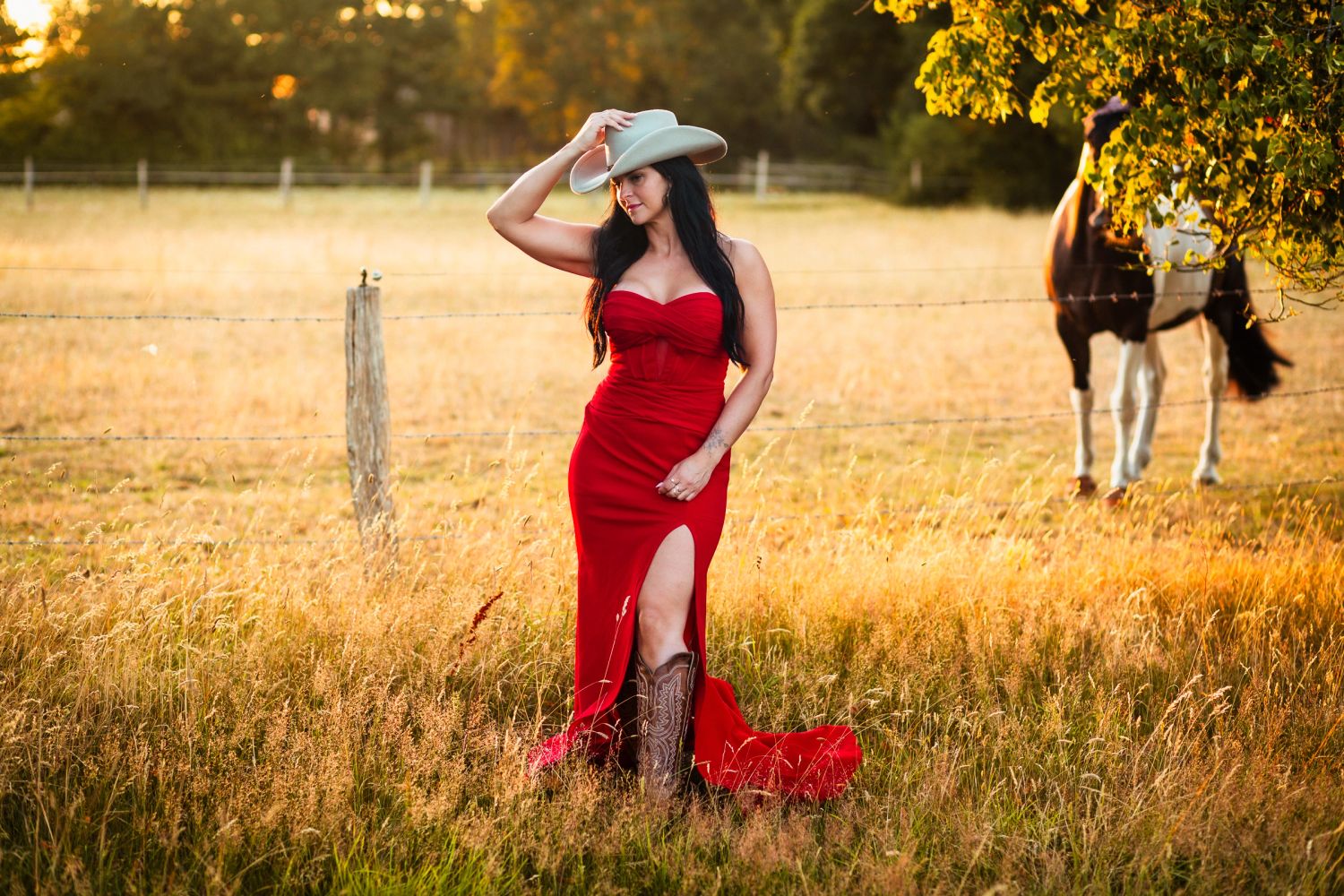 Woman in red dress and cowboy hat in field with horse.