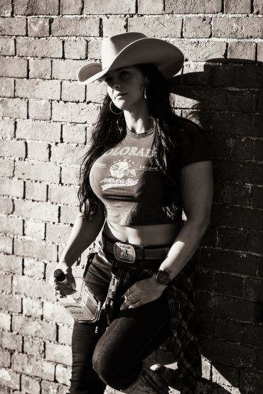 Woman in cowboy hat standing against brick wall with bottle.
