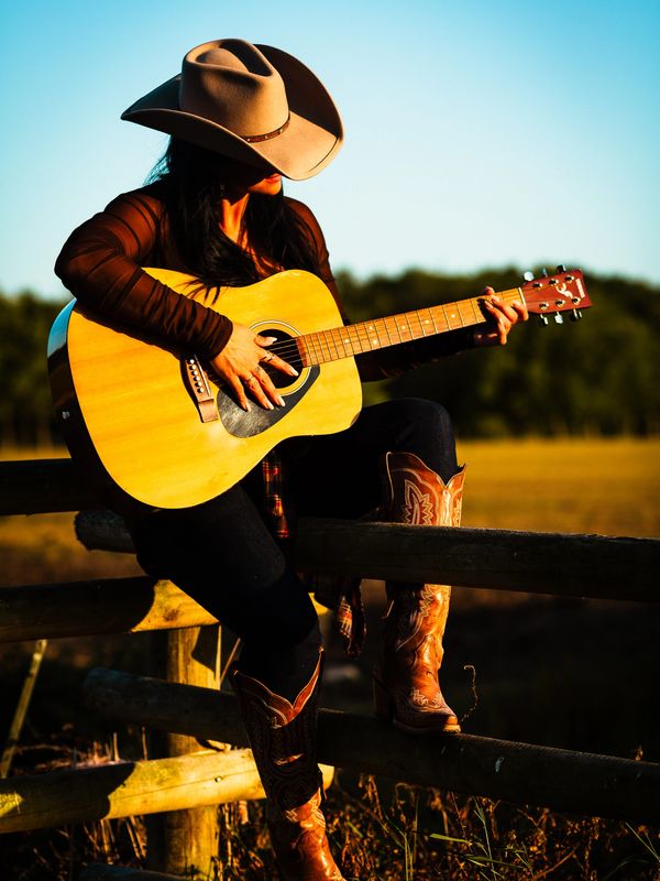 Woman in cowboy hat playing guitar outdoors.