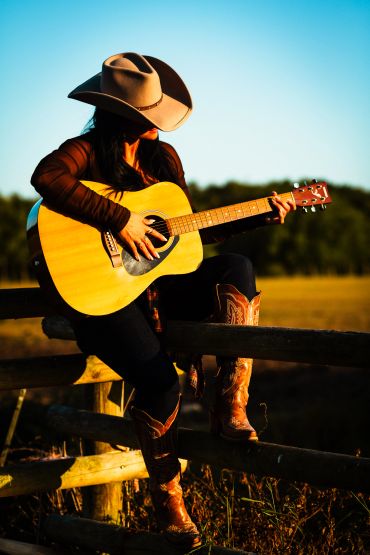Woman in cowboy hat playing acoustic guitar outdoors.