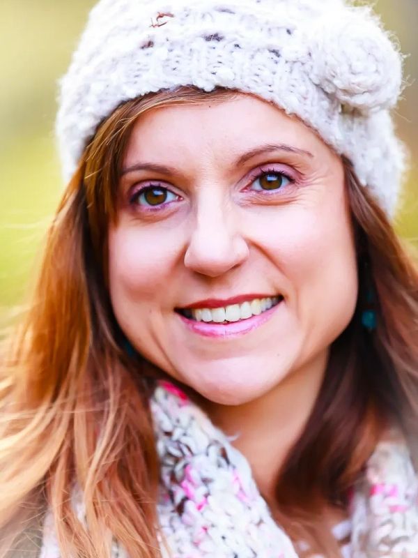Woman smiling outdoors wearing a knit hat and scarf.