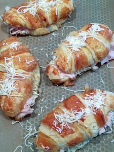 Four croissant sandwiches with shredded cheese on top.