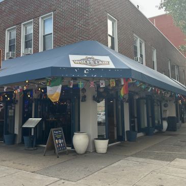 Corner pub with a blue awning and international flags.