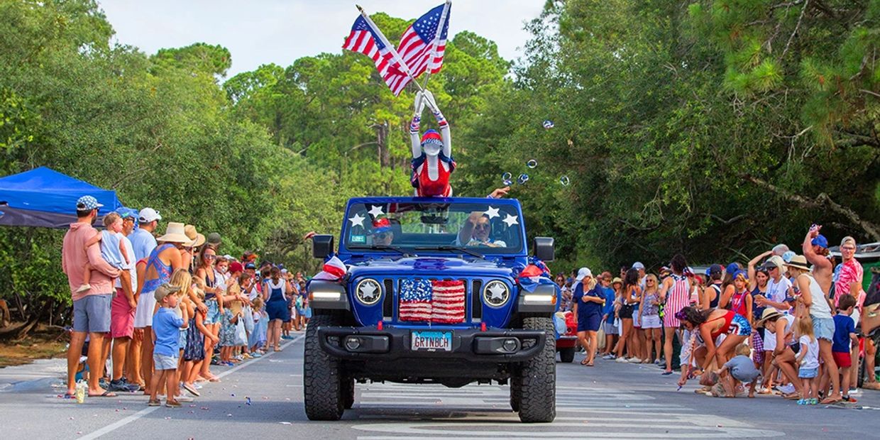 A patriotic parade with a decorated Jeep and people watching along the street.
