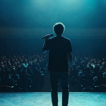 A person holding a microphone stands on stage facing a large audience.