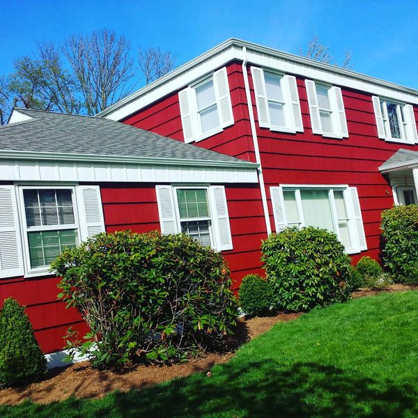 Red house with white shutters and green bushes under a clear blue sky.