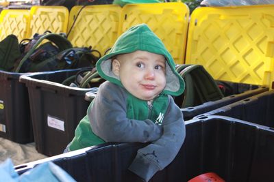Young child in a green hoodie leaning on a container.