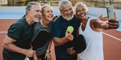 Four seniors happily taking a selfie on a pickleball court.