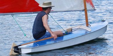 A man in a hat sails a small boat on calm water.