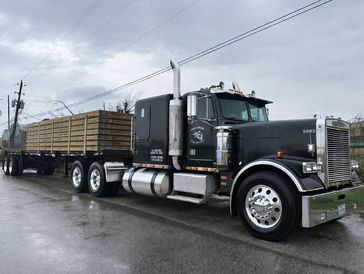 Black Freightliner semi truck with wooden flatbed trailer on a wet road.