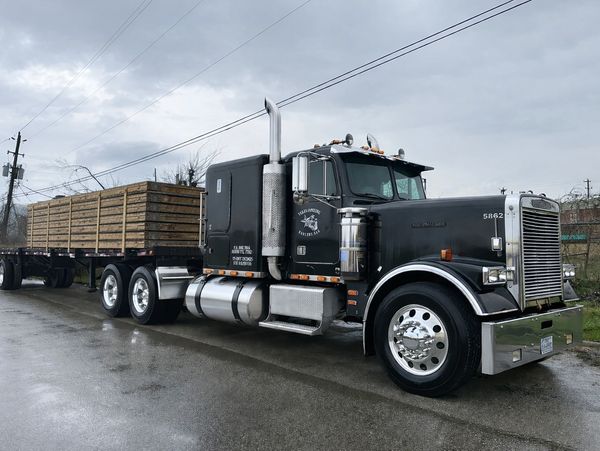 Black semi-truck with wooden cargo on a rainy day.