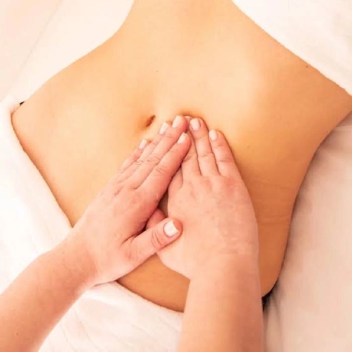 Hands performing a stomach massage on a person lying down.