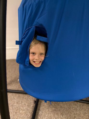 Child peeking through a hole in blue fabric with a smile.