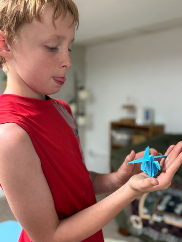 Boy in red shirt examining a blue origami figure.