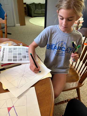 Girl drawing zentangle patterns at a table.