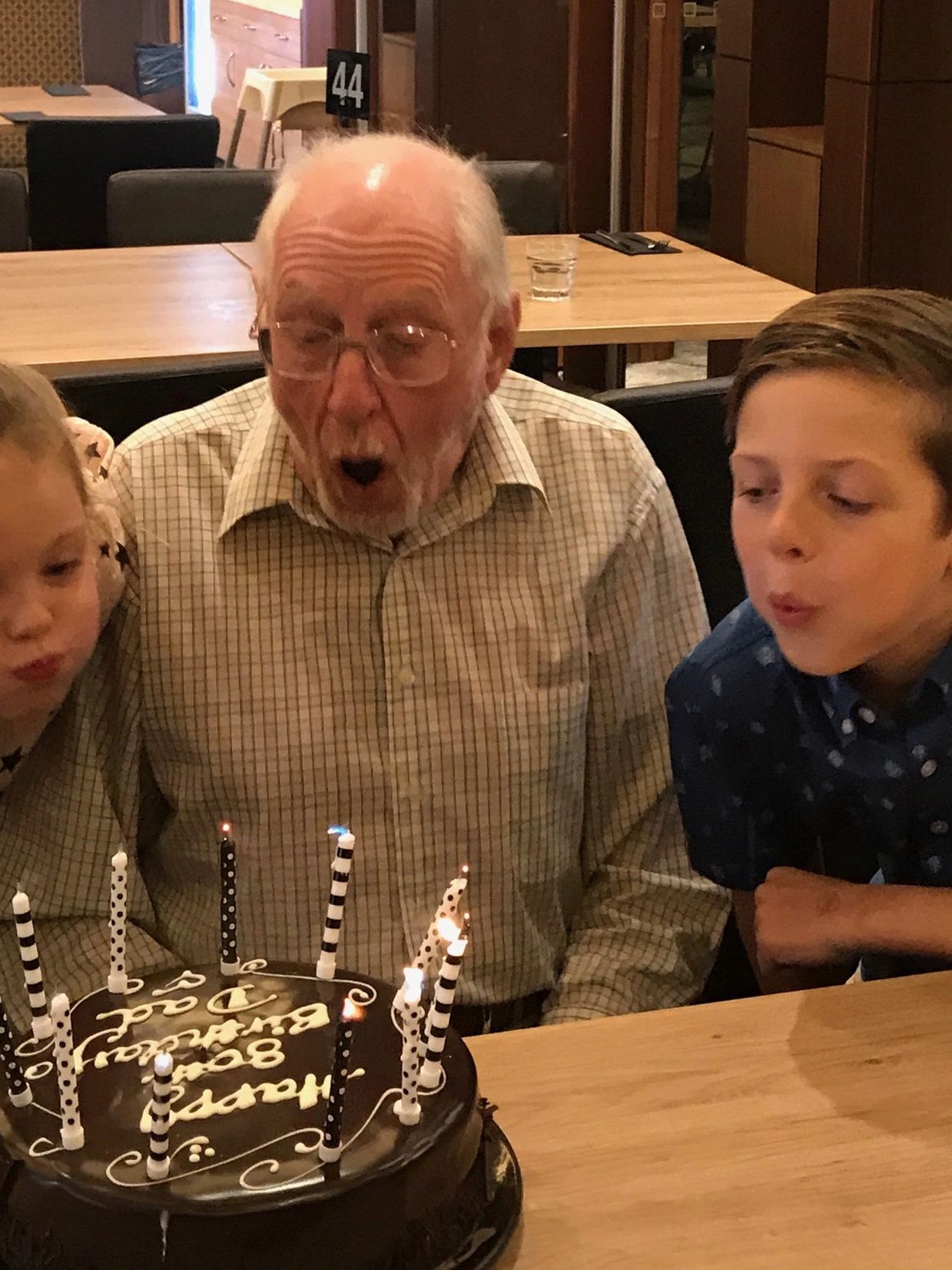 A man celebrates his 80th birthday with his grandchildren by blowing out candles on a birthday cake