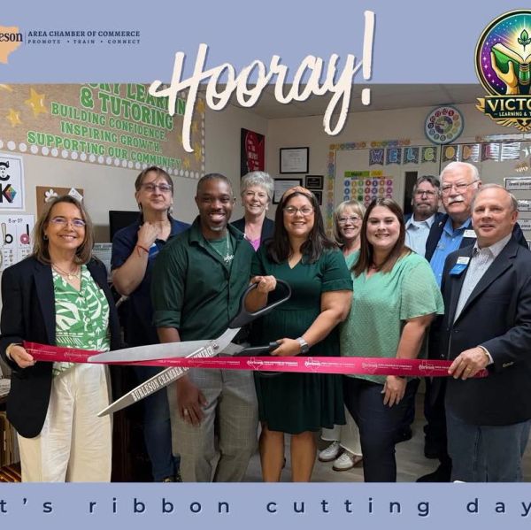 Group celebrates ribbon cutting with large scissors.