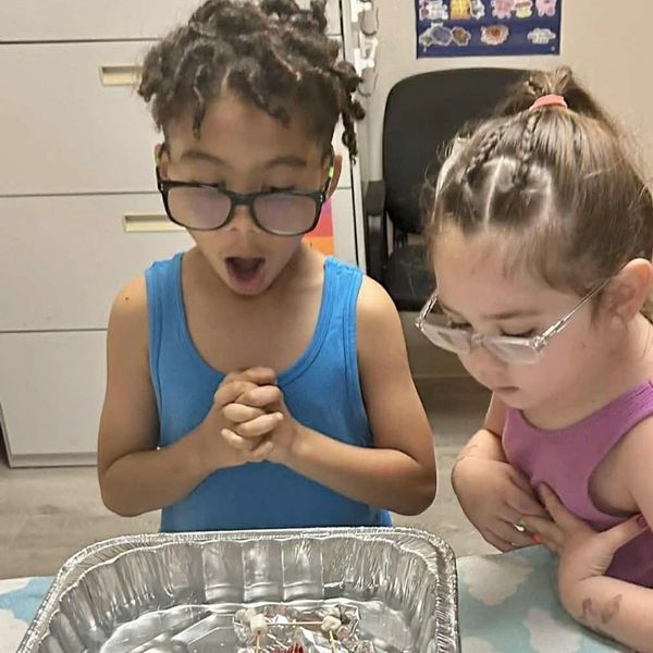 Two children with glasses excitedly looking at a foil tray with items inside.