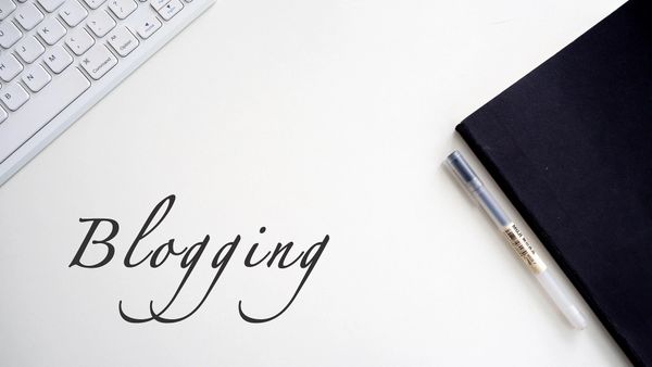 A professional office desk featuring a keyboard, a laptop, and a sign reading "blogging".
