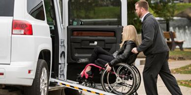 A man assists a woman in a wheelchair onto a vehicle via a ramp.