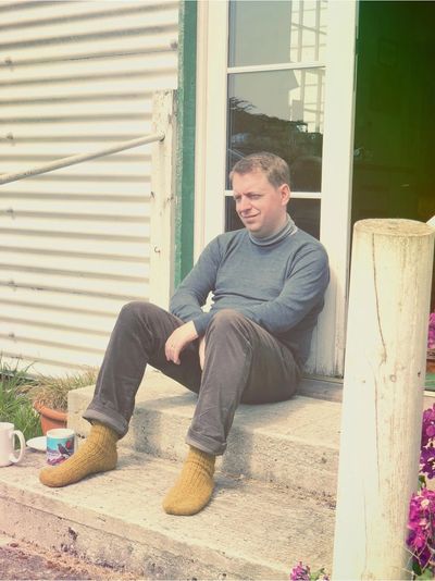 A photograph of me, Neil, the weaver sat on the steps of a house in the Falkland Islands