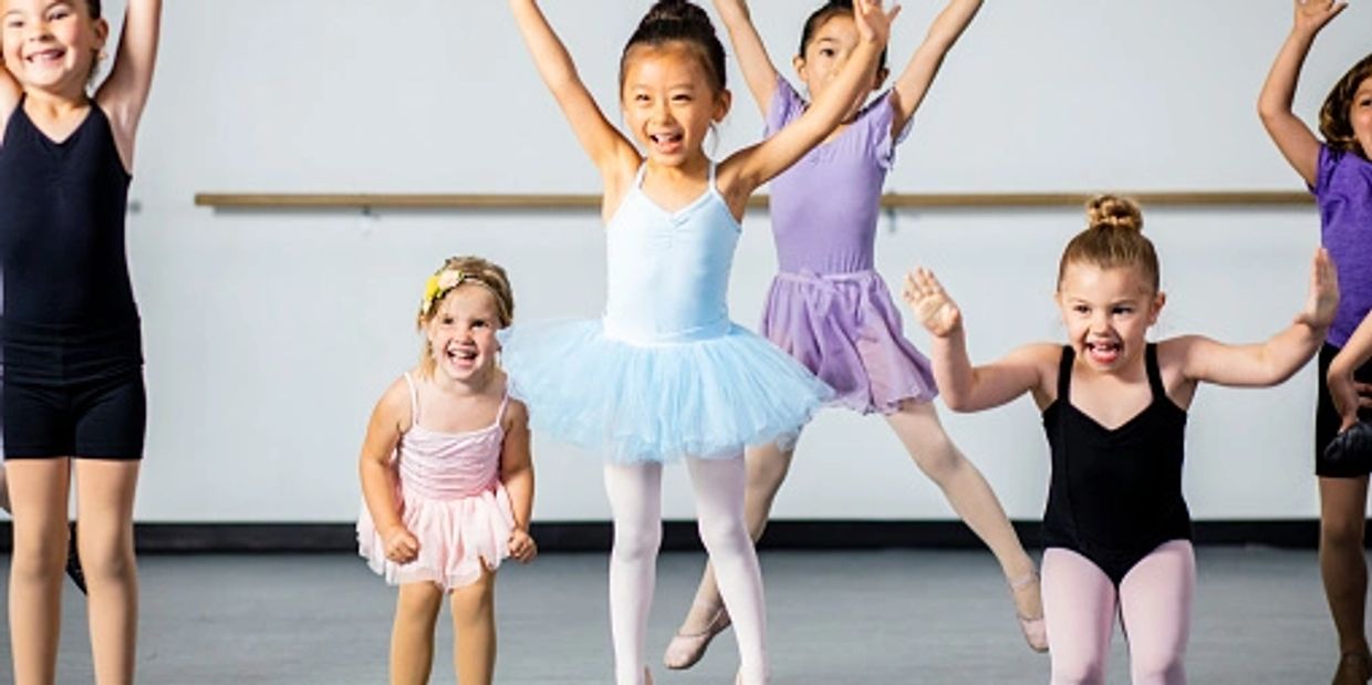 Happy children in ballet outfits jumping in dance class.
