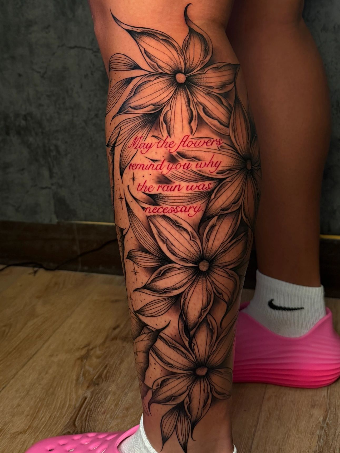 Leg tattoo of flowers with a quote in red ink.