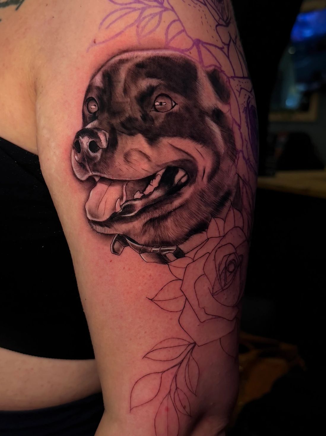 Realistic dog tattoo with floral outlines on arm.