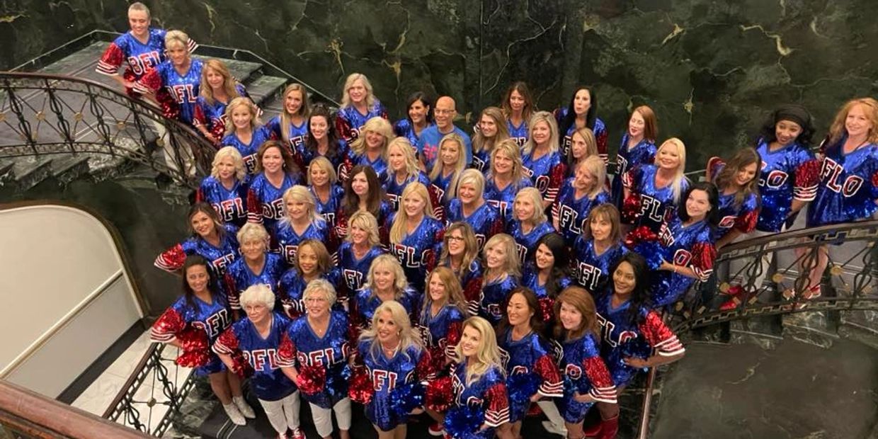 Large group of women in matching blue and red cheerleading outfits posing on a staircase.