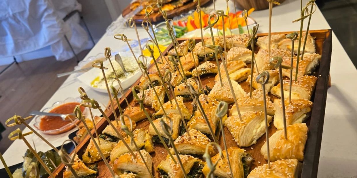 Tray of assorted pastry appetizers with sesame seeds and skewers.