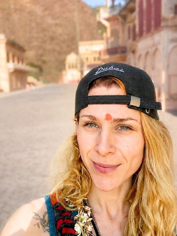 Woman with blonde hair and a black cap stands smiling outdoors.
