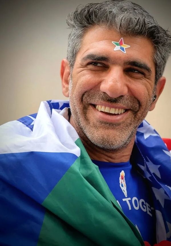 Man smiling with colorful star sticker on forehead, wrapped in a blue, white, and green flag.