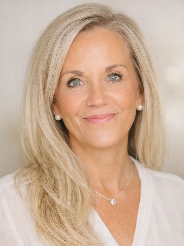 Smiling woman with blonde hair, pearl earrings, and a delicate necklace.