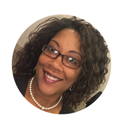 Smiling woman with curly hair, glasses, and a pearl necklace.