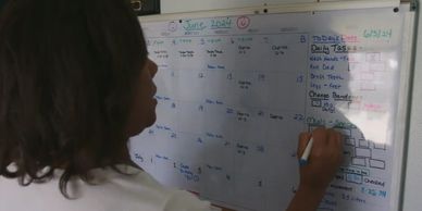Person writing on a whiteboard calendar with daily tasks.