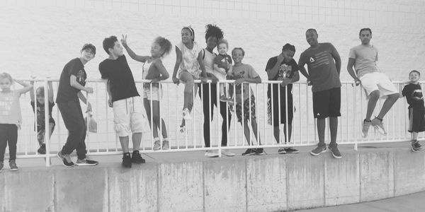 Group of diverse people posing playfully on a railing outdoors.