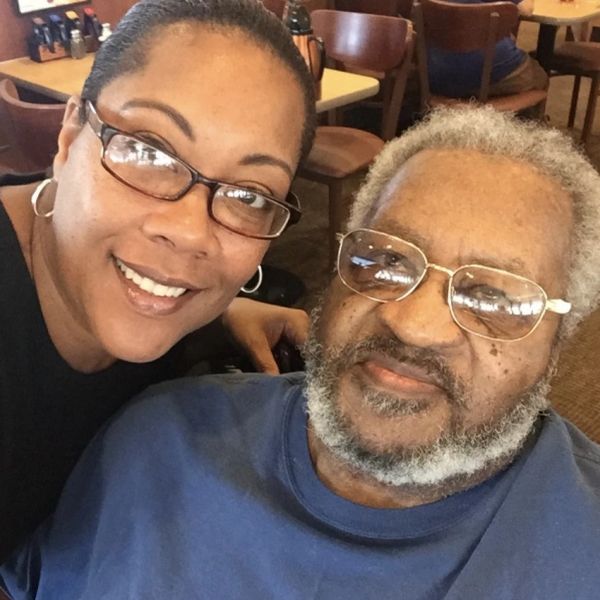 Smiling woman and elderly man wearing glasses pose together indoors.