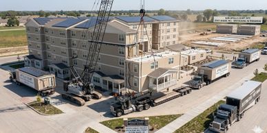 Crane assembling a modular hotel building with transport trucks nearby.