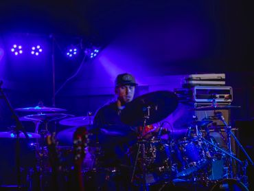 Drummer playing on stage under blue lights.
