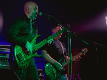 Two musicians playing guitars on stage under purple lights.