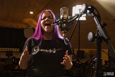 Woman singing passionately into a microphone in a studio.