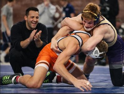 High-intensity wrestling match with athletes executing advanced techniques under coach supervision.