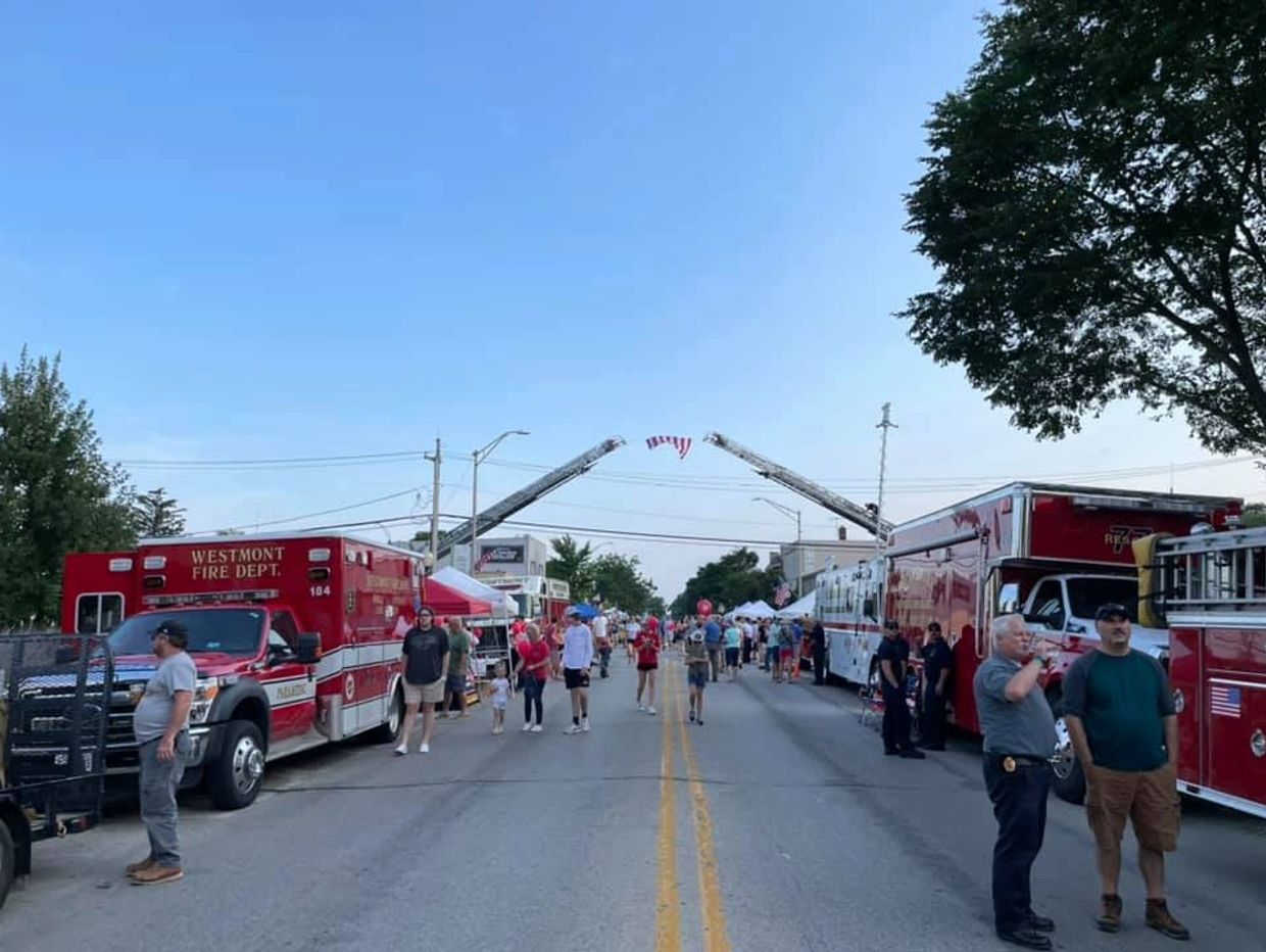 Community event with fire trucks and people gathered under a clear blue sky.
