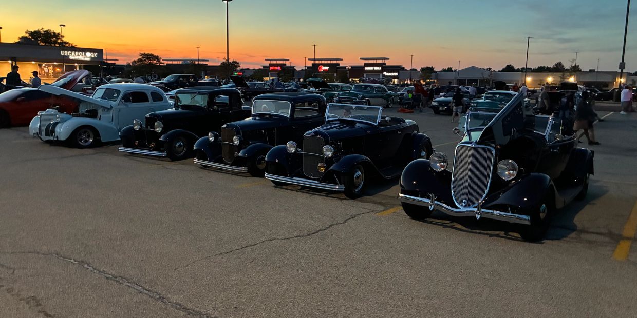 Vintage cars lined up at sunset in a parking lot.