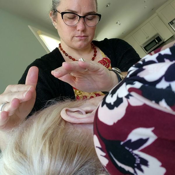 Person with eyes closed, hands above a person's head giving Reiki healing energy