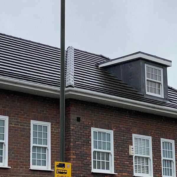 Brick building with white-framed windows and a dormer under a gray sky.