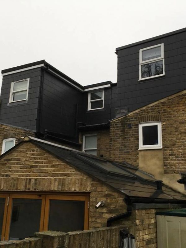 Brick house with black upper extensions and multiple windows.