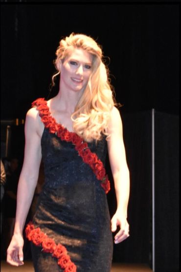 Woman in black dress with red rose accents on runway.
