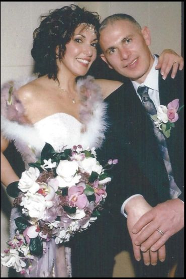 Bride and groom posing happily with wedding attire and bouquet.
